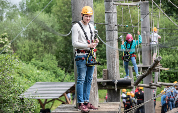 Junger Mann mit Sicherung  und Helm steht auf einer Plattform im Kletterpark